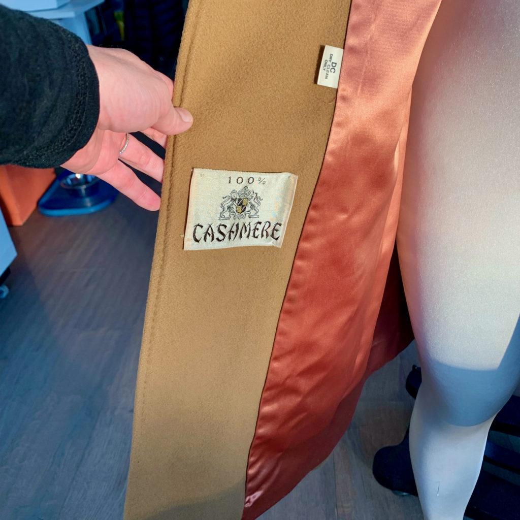 Inside the front of a camel cashmere coat showing the content label and laundering instructions